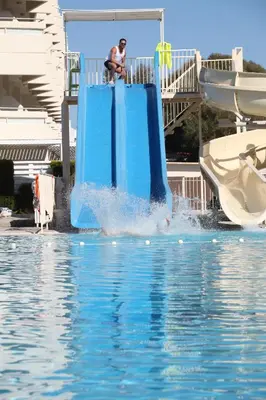a man on a blue slide in the water at Delfinia Resort - All Inclusive in Kolimbia