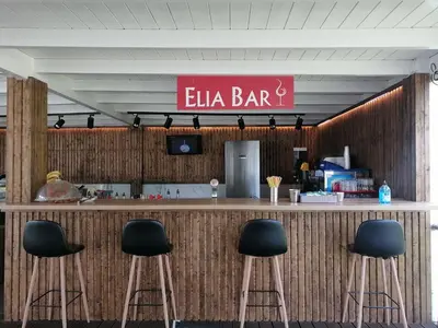 a bar with four stools in front of it with a sign at Delfinia Resort - All Inclusive in Kolimbia