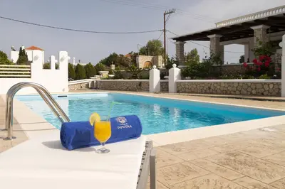 a glass of wine sitting on a table next to a swimming pool at Villa Dimitra Gennadi in Gennadi