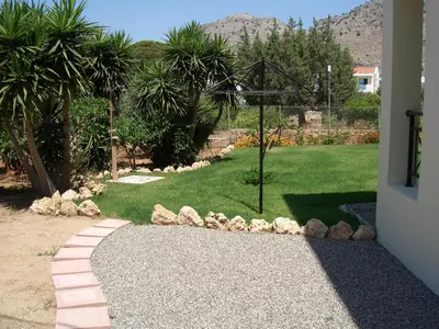 a garden with a walkway and a lawn with palm trees at Sifis Studios Pefkos in Pefki Rhodes