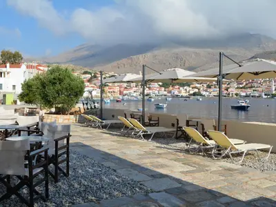 a group of tables and chairs with umbrellas and a body of water at Aretanassa Hotel in Halki