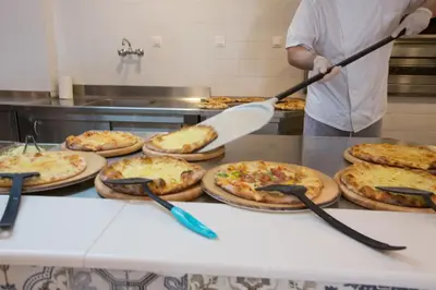 a man holding a spatula over a table with pizzas at Sun Palace Hotel in Faliraki
