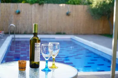 a bottle of wine and two glasses on a table near a swimming pool at The Blue Leaf Family Villa in Gennadi