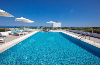 a swimming pool with chairs and umbrellas on a building at Aegean Horizon Beachfront Villas in Gennadi