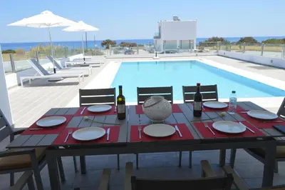 a table with plates and wine bottles next to a swimming pool at Aegean Horizon Beachfront Villas in Gennadi