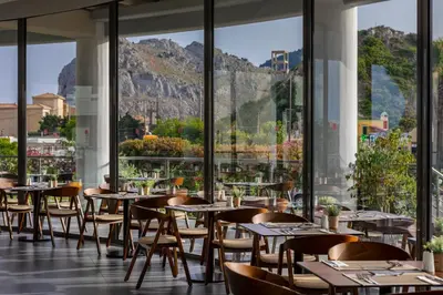 a restaurant with tables and chairs with mountains in the background at Leonardo Kolymbia Resort Rhodes in Kolimbia