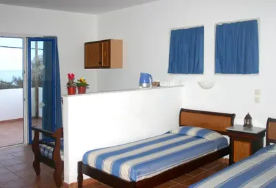 a bedroom with a bed and a window with blue curtains at Katikies Studios & Apartments in Lardos