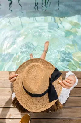 a woman wearing a straw hat sitting next to a swimming pool at Caesars Gardens Hotel & Spa - Adults Only in Líndos