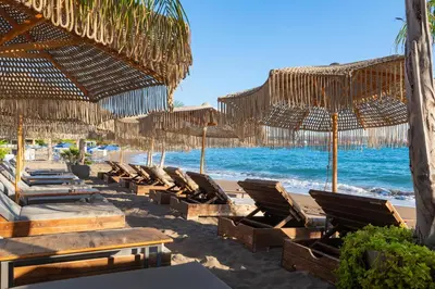 a beach with chairs and straw umbrellas and the ocean at Aquarius Beach Hotel in Faliraki