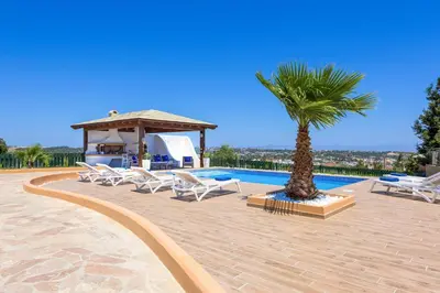 a group of chairs and a palm tree next to a pool at Aegean Blue Villa in Koskinou