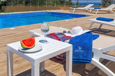 a white table with a glass of wine and a slice of watermelon at Aegean Blue Villa in Koskinou