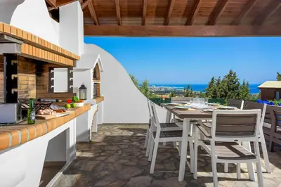 an outdoor kitchen with a table and chairs on a patio at Aegean Blue Villa in Koskinou
