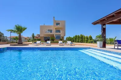 a swimming pool with chairs and a house in the background at Aegean Blue Villa in Koskinou
