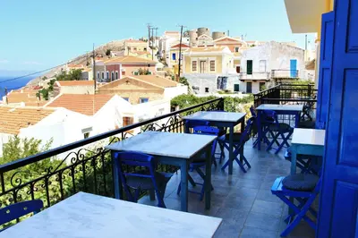 a patio with tables and chairs on a balcony at Hotel Fiona Symi in Symi