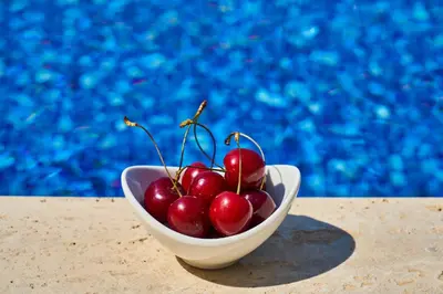 a bowl of cherries sitting on a table next to a pool at GOJI Vegan Hotel in Ialyssos