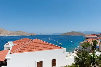 a white building with a red roof next to the water at Atlantis Houses in Halki
