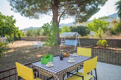 a table with yellow chairs in a backyard with a tree at Country House in Pastida