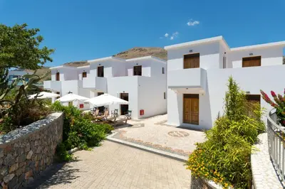 a row of white buildings with tables and umbrellas at George's Villas in Líndos