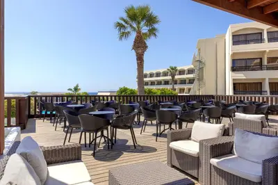a deck with chairs and tables and a palm tree at Sol Cosmopolitan Rhodes in Ixia