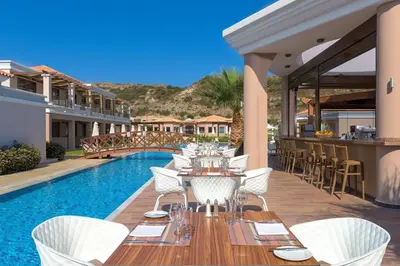 a patio with a table and chairs next to a pool at La Marquise Luxury Resort Complex in Faliraki