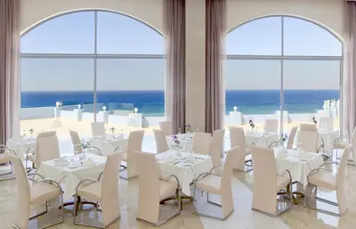 a dining room with white tables and chairs and the ocean at Atrium Platinum Resort & Spa in Ixia