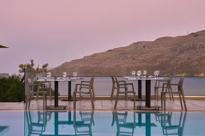 a table with wine glasses and chairs next to a pool at Lindos Royal Resort in Líndos