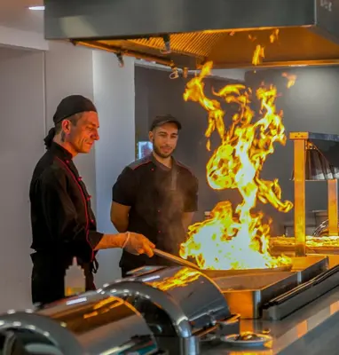 two men standing in a kitchen cooking food on a grill at Akti Imperial Deluxe Resort & Spa Dolce by Wyndham in Ixia
