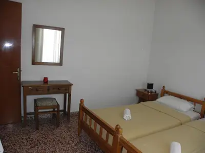 a bedroom with two beds and a table and a mirror at Afroditi Pension in Archangelos