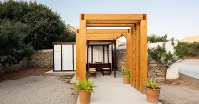 a wooden pavilion with a table and chairs under it at Pedi Beach Hotel in Symi