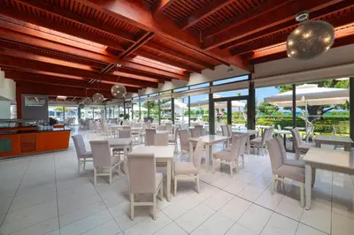 a restaurant with white tables and chairs and windows at All Senses Ocean Blue Sea Side Resort - All Inclusive in Kremasti