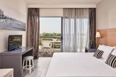 a hotel room with a bed and a television and a balcony at All Senses Ocean Blue Sea Side Resort - All Inclusive in Kremasti