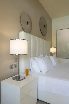 a bedroom with a white bed with a lamp and pillows at All Senses Ocean Blue Sea Side Resort - All Inclusive in Kremasti