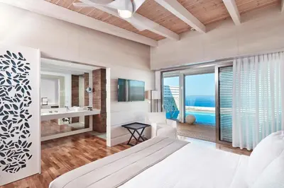 a bedroom with a bed and a bathroom with a view of the ocean at Esperos Village Blue & Spa - Adults Only in Faliraki