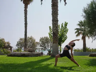 a woman doing a yoga pose in a park with palm trees at Esperos Village Blue & Spa - Adults Only in Faliraki