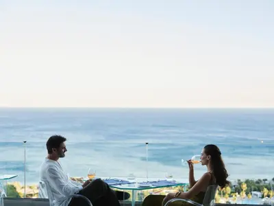 a man and woman sitting on a balcony with a view of the ocean at Esperos Village Blue & Spa - Adults Only in Faliraki