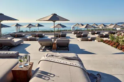 a row of lounge chairs and umbrellas on a beach at Esperos Village Blue & Spa - Adults Only in Faliraki