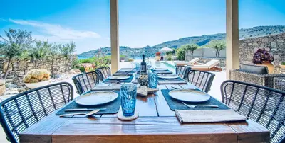 a long wooden table with plates and glasses on it at Villa Lindos Kalliopi on Rhodes AMA 0 0 0 0 3 6 6 0 4 0 3 in Líndos