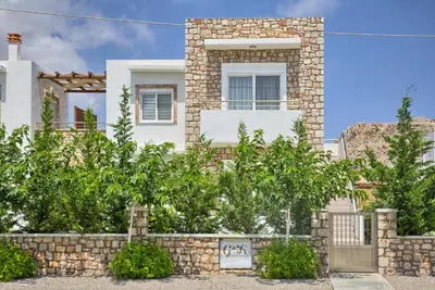 a white house with a stone wall and trees at G&K Stone Suites in Haraki