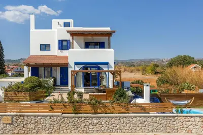 a white house with blue doors and a yard at Villa Rose on the beach in Afantou