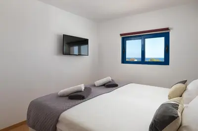 a white bedroom with a bed and a window at Villa Rose on the beach in Afantou
