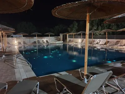 a large swimming pool with chairs and umbrellas at night at Saint George Resort in Archangelos