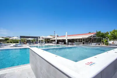 a pool at a resort with tables and chairs at Tsampika Hotel Faliraki in Faliraki