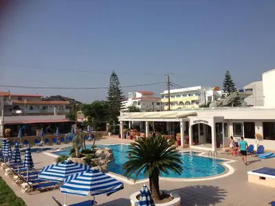 a swimming pool with blue and white umbrellas and buildings at Rhodian Rose Hotel in Faliraki