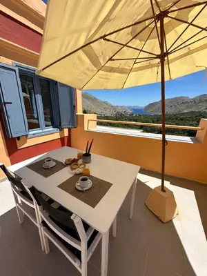 a white table with chairs and an umbrella on a balcony at Taxiarchis in Symi