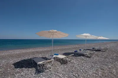 two beach chairs and umbrellas on a rocky beach at Aegiali Sea View Villa in Gennadi