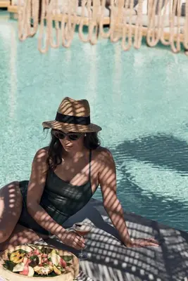 a woman in a hat sitting in front of a pool at Casa Cabana Boutique Hotel & Spa - Adults Only in Faliraki