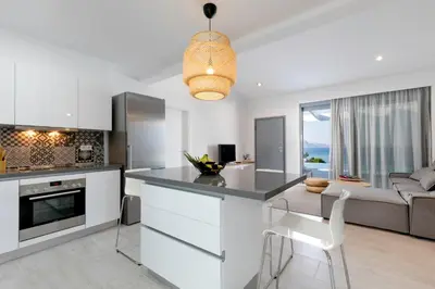 a kitchen and living room with white cabinets and a couch at Villa Serene with swimming pool in Lindos in Líndos