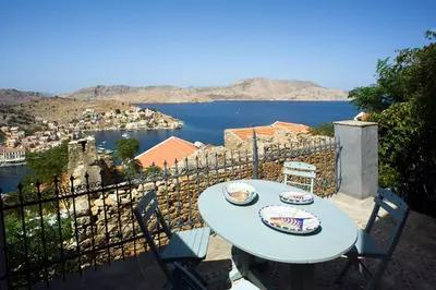 a table and chairs on a balcony with a view of the water at Villa Ricolas in Symi