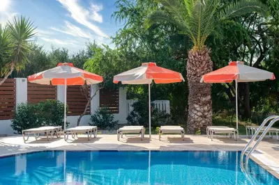 a swimming pool with two umbrellas and chairs and a swimming pool at Meliton Hotel in Theologos