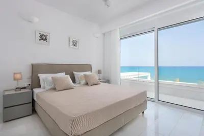 a white bedroom with a bed and a large window at Maria & Nada Beachfront Villas in Kolimbia